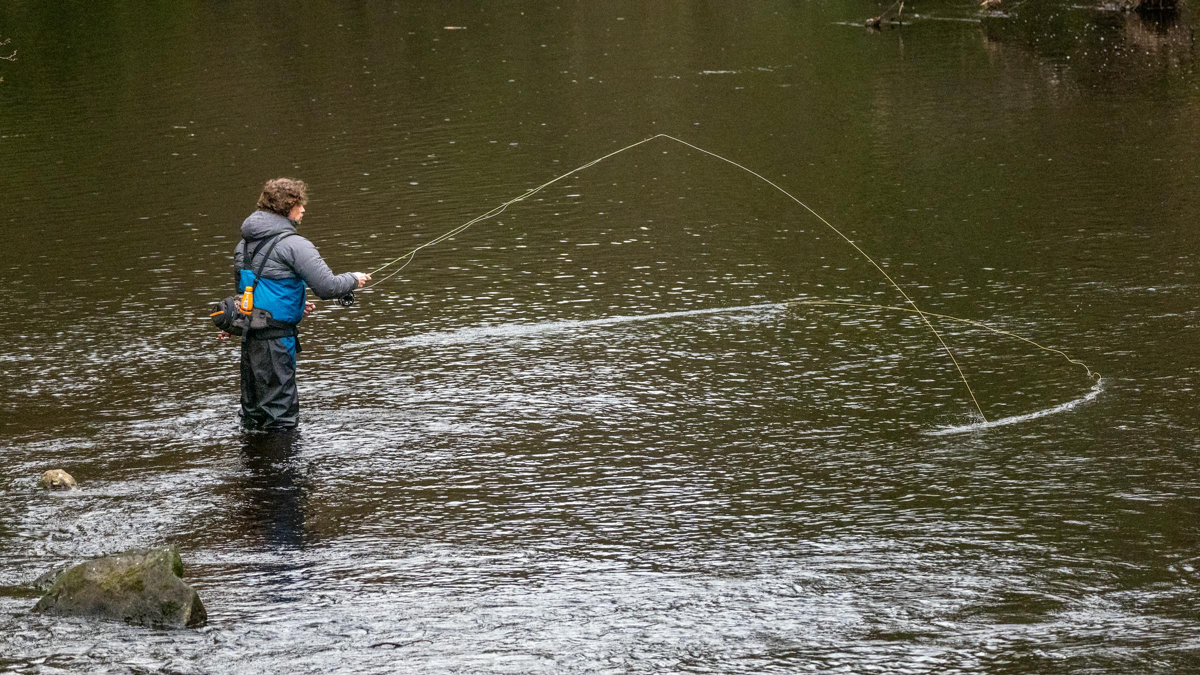 A fly fisherman casting on a quiet river
