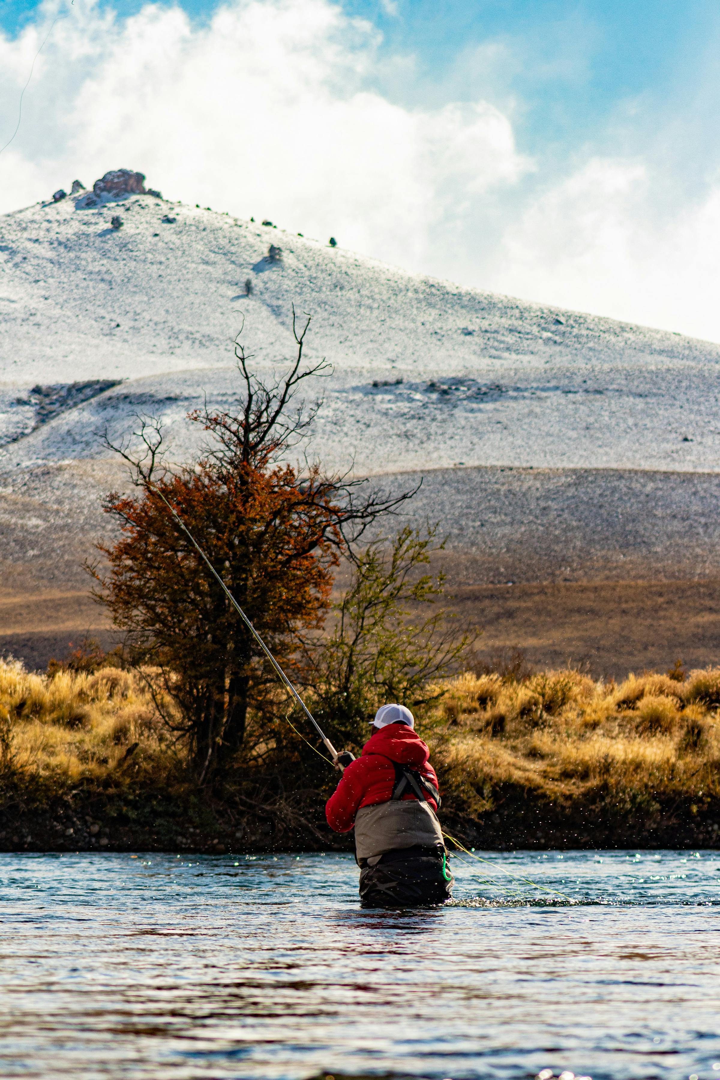 A fly fisherman in a remote landscape with snow-dusted peaks